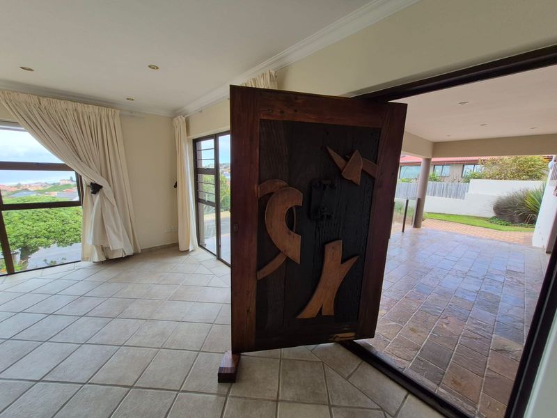 An entrance area featuring a unique wooden pivot door, tiled flooring, and seamless transition to a covered outdoor patio space.