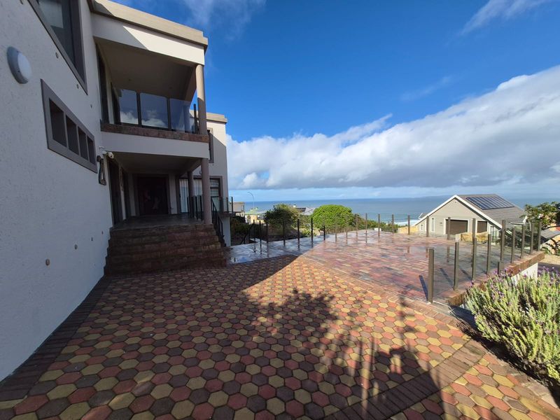 Spacious rear paved patio area featuring glass balustrades and a covered balcony, offering elevated views of the surrounding landscape and ocean.