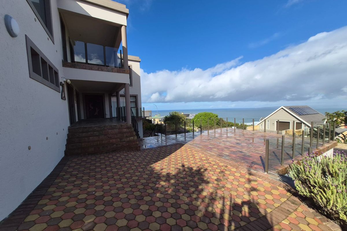Spacious rear paved patio area featuring glass balustrades and a covered balcony, offering elevated views of the surrounding landscape and ocean.