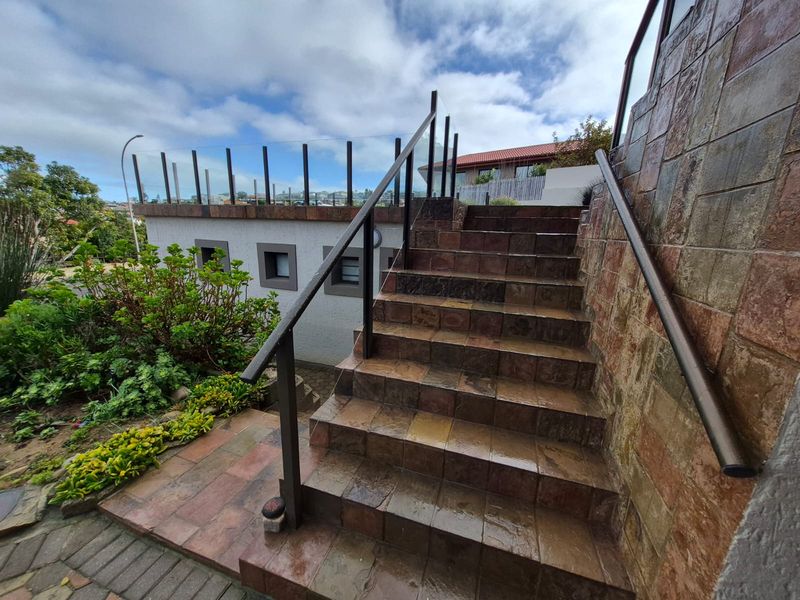 Exterior staircase featuring tiled steps, stone cladding, and a modern glass balustrade leading to an elevated outdoor area.