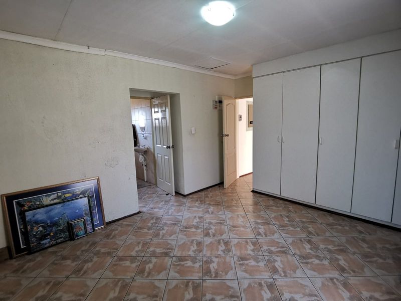 A spacious bedroom featuring built-in cupboards, tiled flooring, and direct access to an en-suite bathroom.