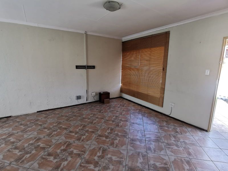 An empty living room featuring tiled flooring, venetian blinds, and wall-mounted electrical fixtures, offering a blank canvas for renovation or interior design.
