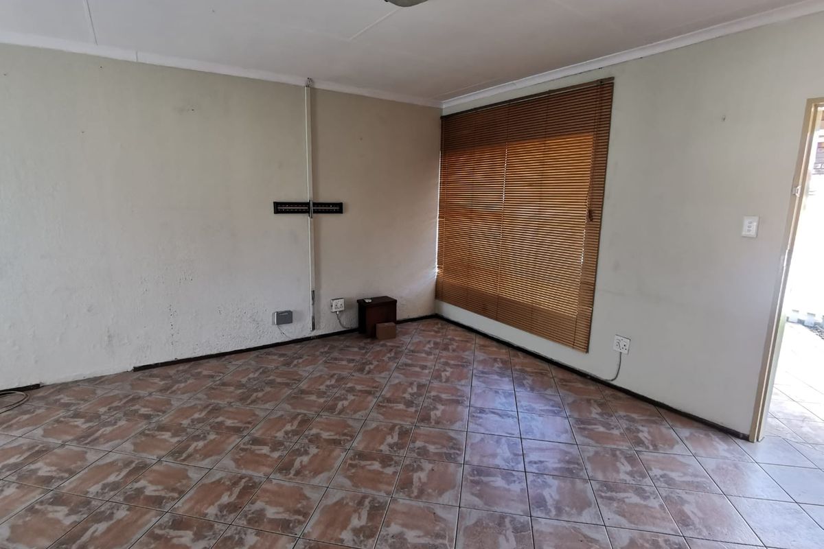 An empty living room featuring tiled flooring, venetian blinds, and wall-mounted electrical fixtures, offering a blank canvas for renovation or interior design.