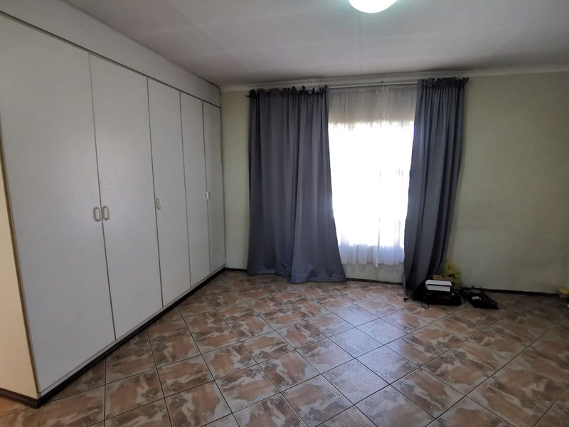 A spacious bedroom featuring built-in cupboards, tiled flooring, and a window with curtains, offering a clean and functional living space.