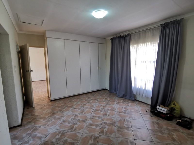 A spacious bedroom featuring built-in cupboards, tiled flooring, and a ceiling access hatch, offering a clean and functional living space.