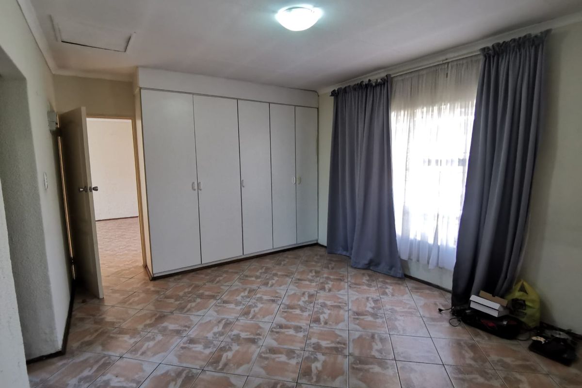A spacious bedroom featuring built-in cupboards, tiled flooring, and a ceiling access hatch, offering a clean and functional living space.