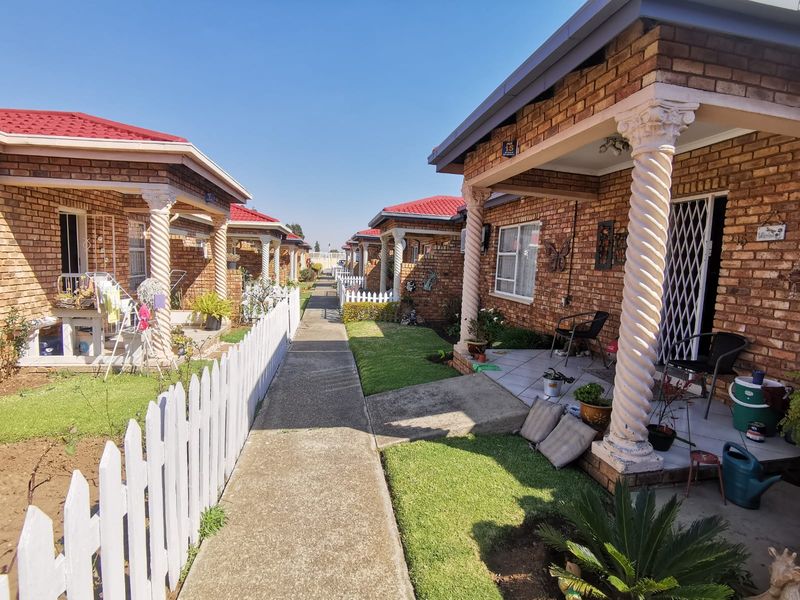 A view of a townhouse complex featuring brick facades, decorative columns, and a central concrete walkway leading through the residential units.