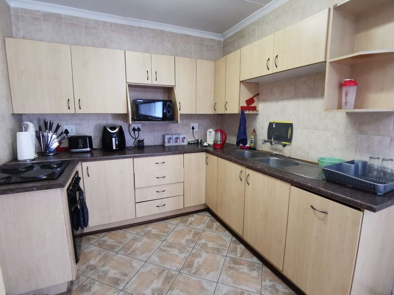 A functional kitchen featuring light wood-look laminate cabinetry, dark countertops, a double stainless steel sink, and ceramic tile flooring.