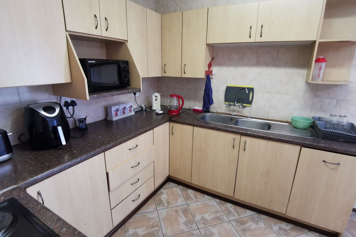 A functional kitchen featuring light wood-tone cabinetry, dark laminate countertops, a double stainless steel sink, and tiled backsplash with ceramic flooring.