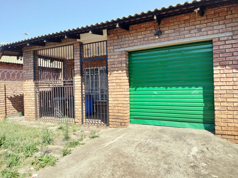 Exterior view of a brick garage featuring a green metal roller door, security gates, and a concrete driveway.