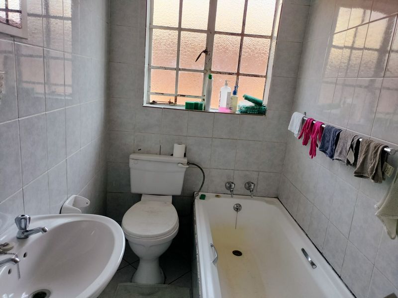 A compact bathroom featuring a standard bathtub, pedestal basin, and toilet with tiled walls and floors, requiring cosmetic updates to improve its condition.