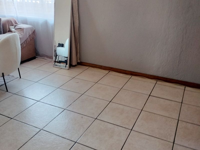 A living area featuring neutral ceramic floor tiles, timber skirting boards, and a window fitted with security bars.