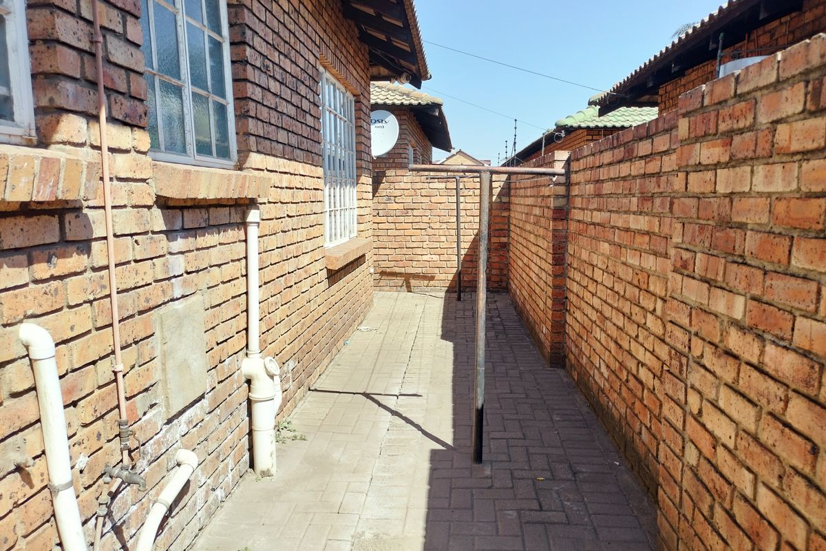 A side exterior walkway featuring brick walls, paved flooring, and a fixed metal washing line.