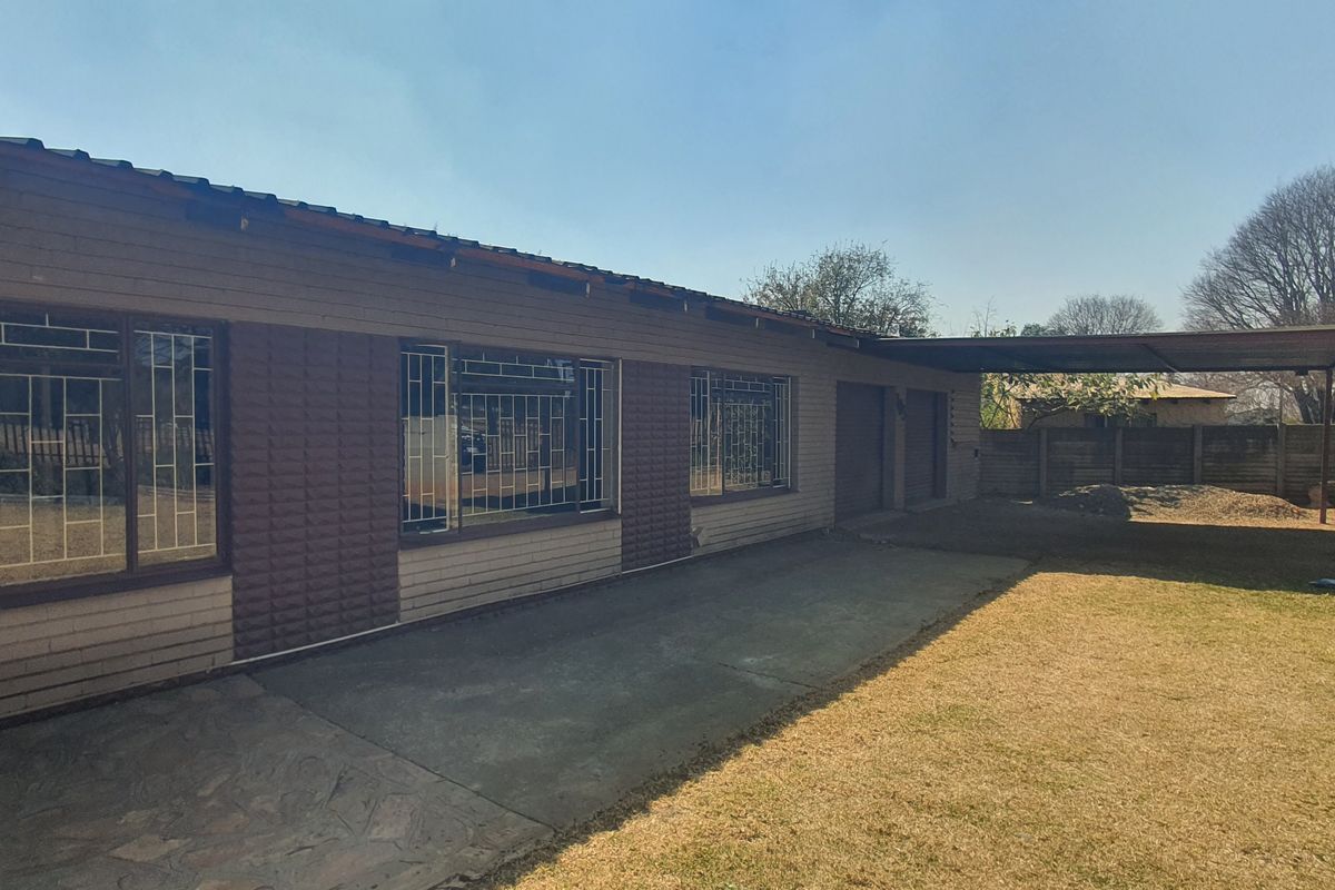 Rear view of the house featuring a brick facade, security bars on windows, a concrete patio area, and an attached carport.