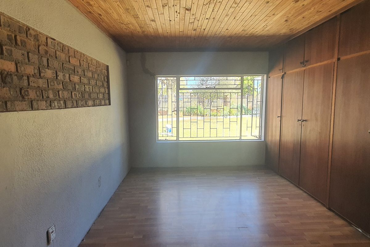 An empty bedroom featuring built-in wooden cupboards, a timber ceiling, laminate flooring, and an exposed brick feature wall with security bars on the window.