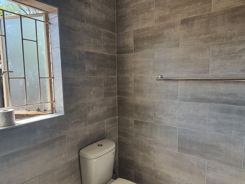 A modern bathroom featuring grey ceramic wall tiles, a toilet, and a window with security bars.