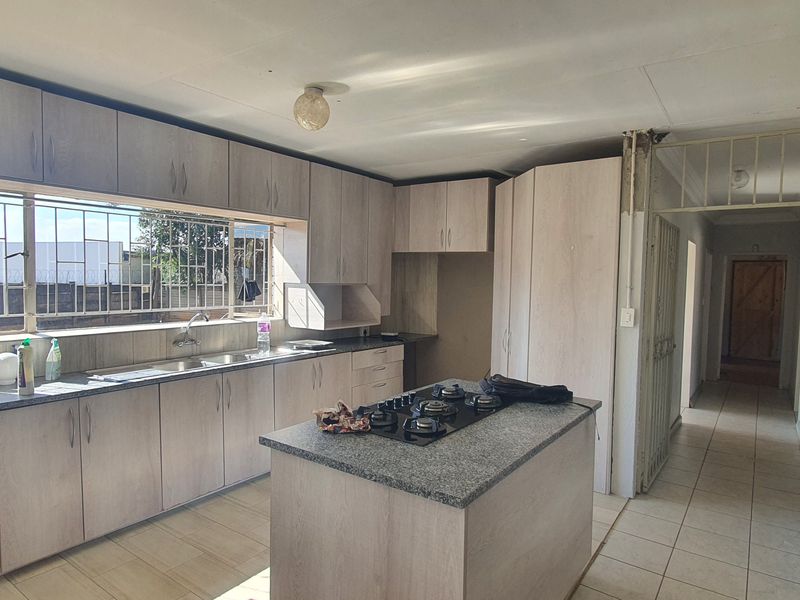 Spacious kitchen featuring light wood-finish cabinetry, granite countertops, a central island with a gas hob, and tiled flooring throughout.