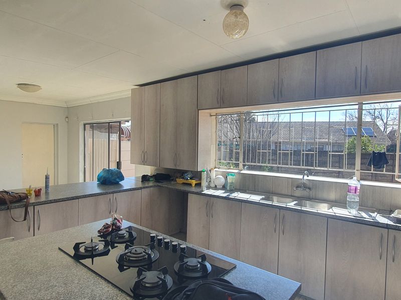 Spacious kitchen featuring light wood-grain cabinetry, granite countertops, a central gas hob, and a double sink with views to the exterior.