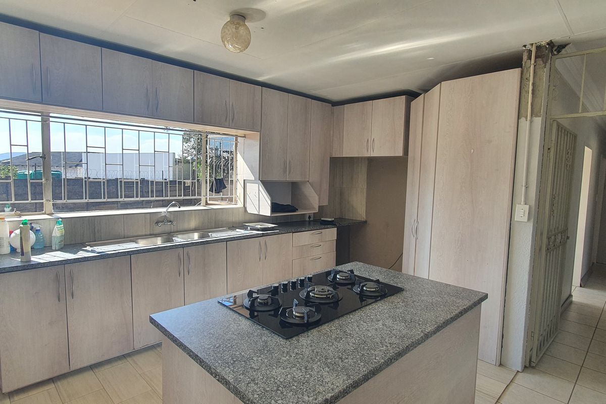 Spacious kitchen featuring light wood-finish cabinetry, granite countertops, a central island with a gas hob, and tiled flooring throughout.