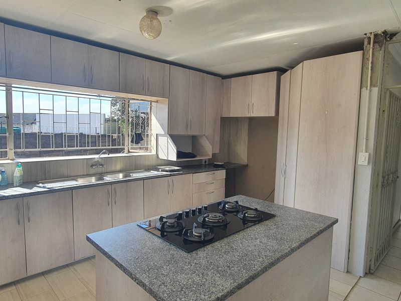 Spacious kitchen featuring light wood-finish cabinetry, granite countertops, a central island with a gas hob, and tiled flooring throughout.