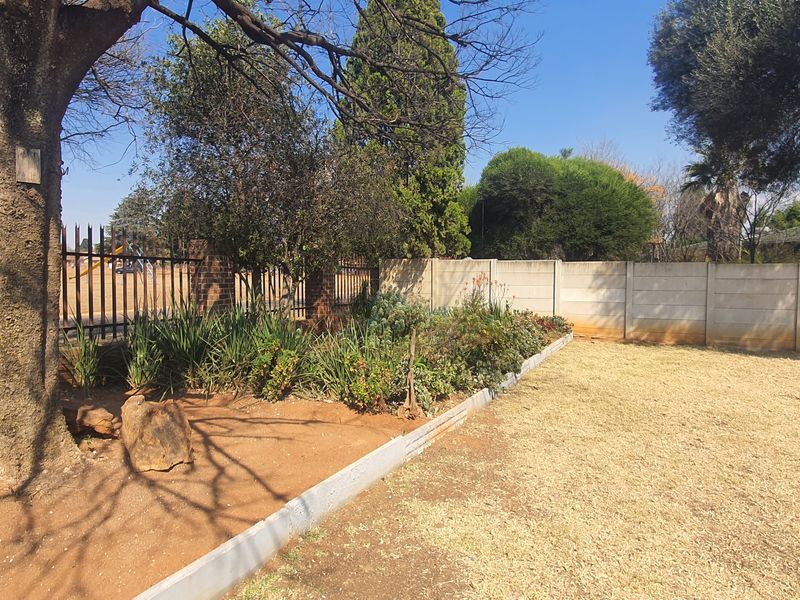 A spacious garden area featuring a precast concrete boundary wall, metal perimeter fencing, and established garden beds with concrete edging.