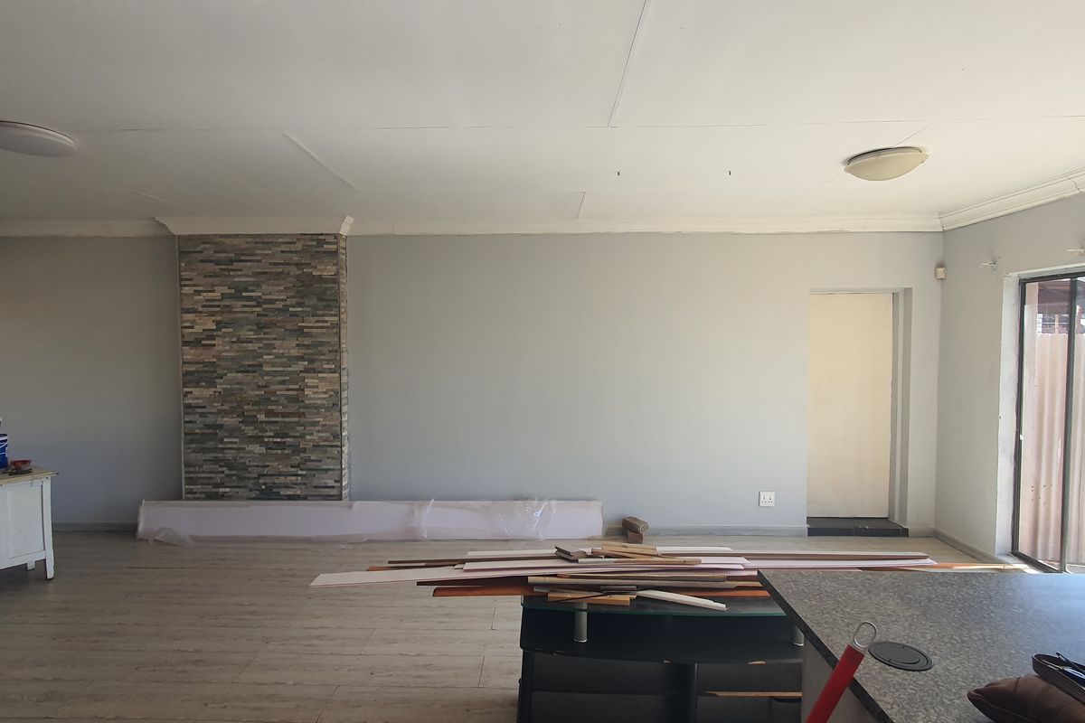Spacious living area featuring a stone accent wall, laminate flooring, and sliding glass doors leading to the exterior. Currently undergoing minor renovations.