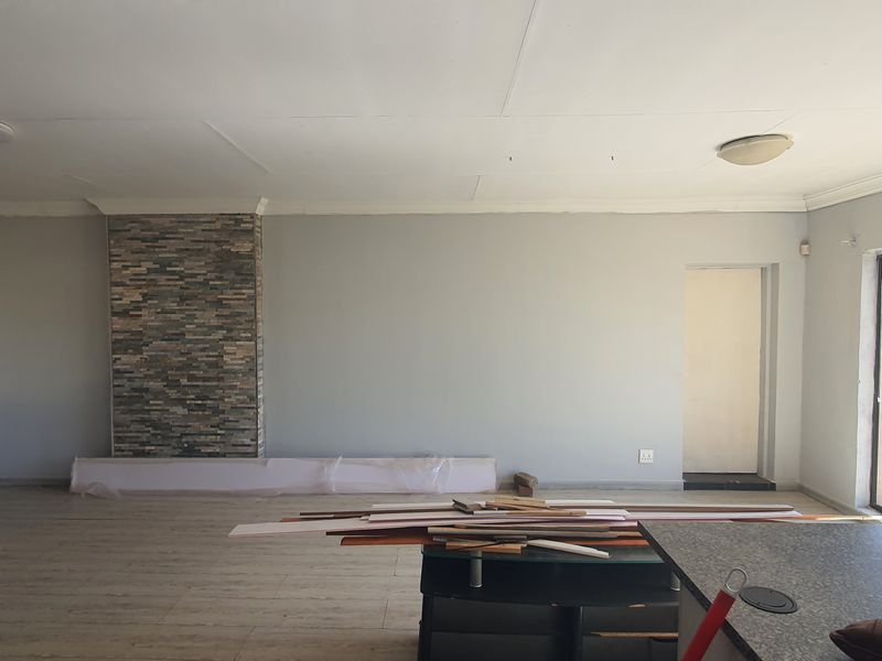 Spacious living area featuring a stone accent wall, laminate flooring, and sliding glass doors leading to the exterior. Currently undergoing minor renovations.