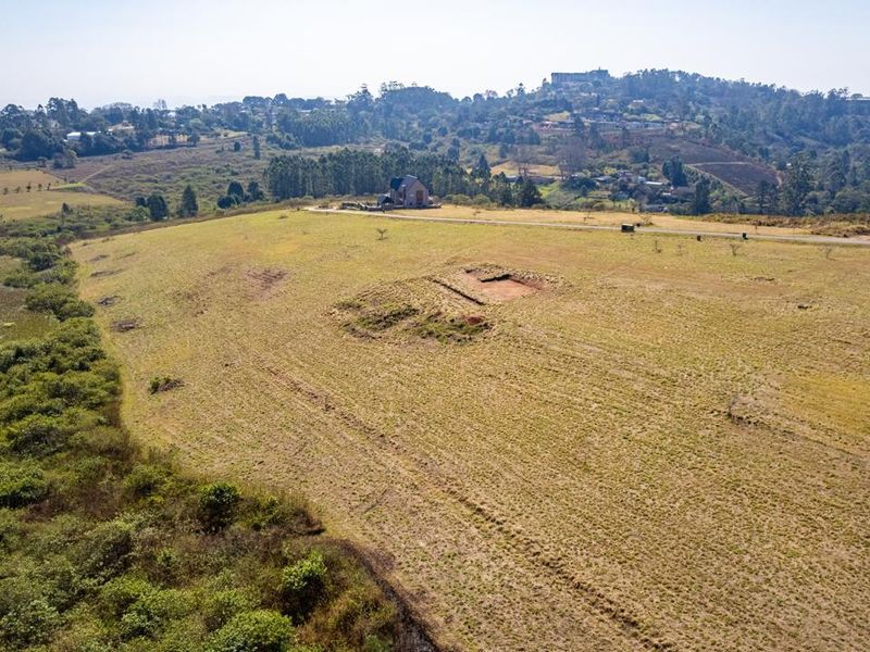 An aerial view of a large, sloping vacant residential plot featuring natural grassland and a small excavated area.