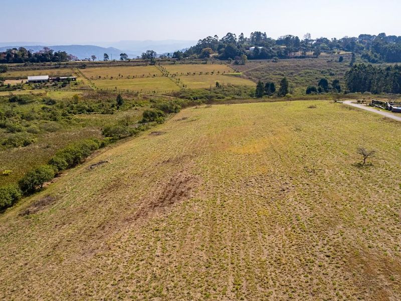 An aerial view of a large, open vacant residential plot featuring natural grassland and surrounding landscape views.