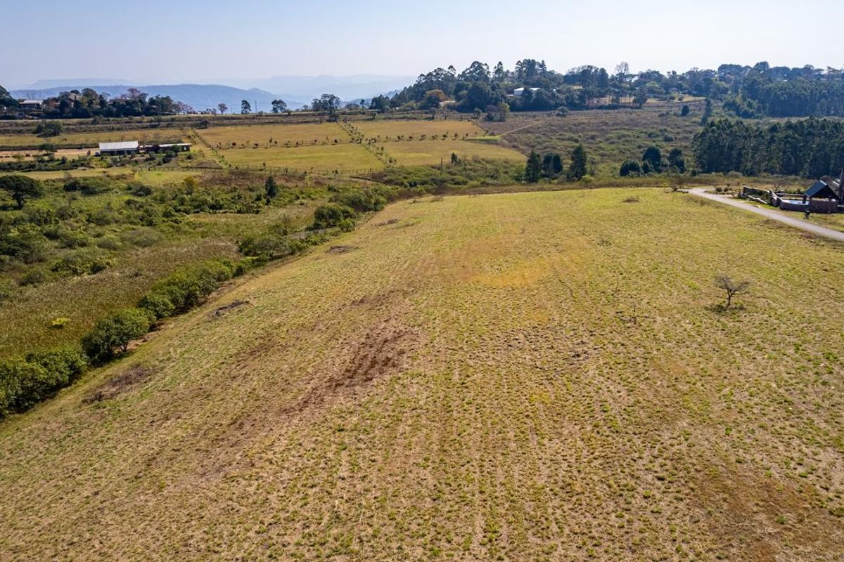 An aerial view of a large, open vacant residential plot featuring natural grassland and surrounding landscape views.