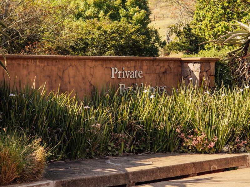 A view of the entrance signage and landscaped boundary wall for the residential property, featuring stone masonry and established garden greenery.