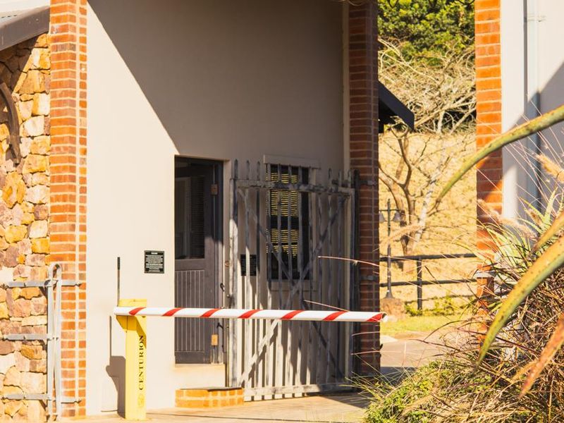 A secure entrance featuring a brick archway, stone cladding, and an automated security boom gate.