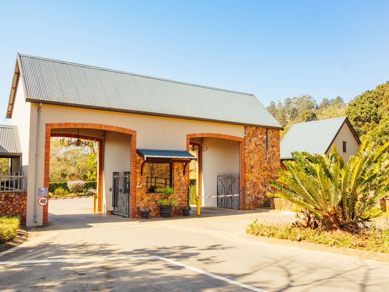 A well-maintained residential estate security gatehouse featuring stone cladding, brick archways, and functional boom gate access.