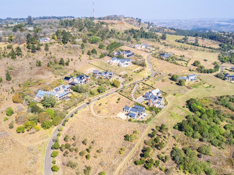 An aerial view of a residential estate featuring multiple homes, paved access roads, and surrounding natural landscape.