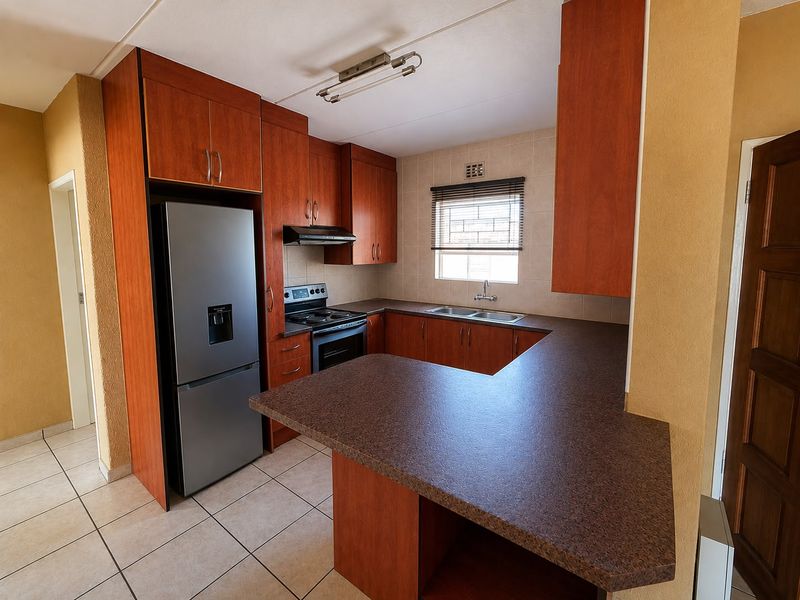 Functional kitchen featuring wood-look cabinetry, laminate countertops, a breakfast nook, and built-in appliances including an oven and extractor fan.