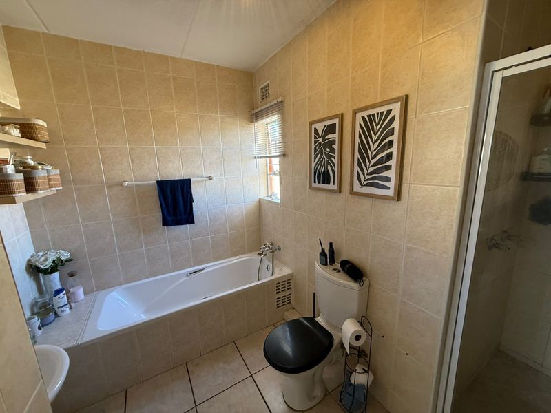 A functional bathroom featuring a built-in bathtub, separate shower enclosure, and neutral wall and floor tiling.