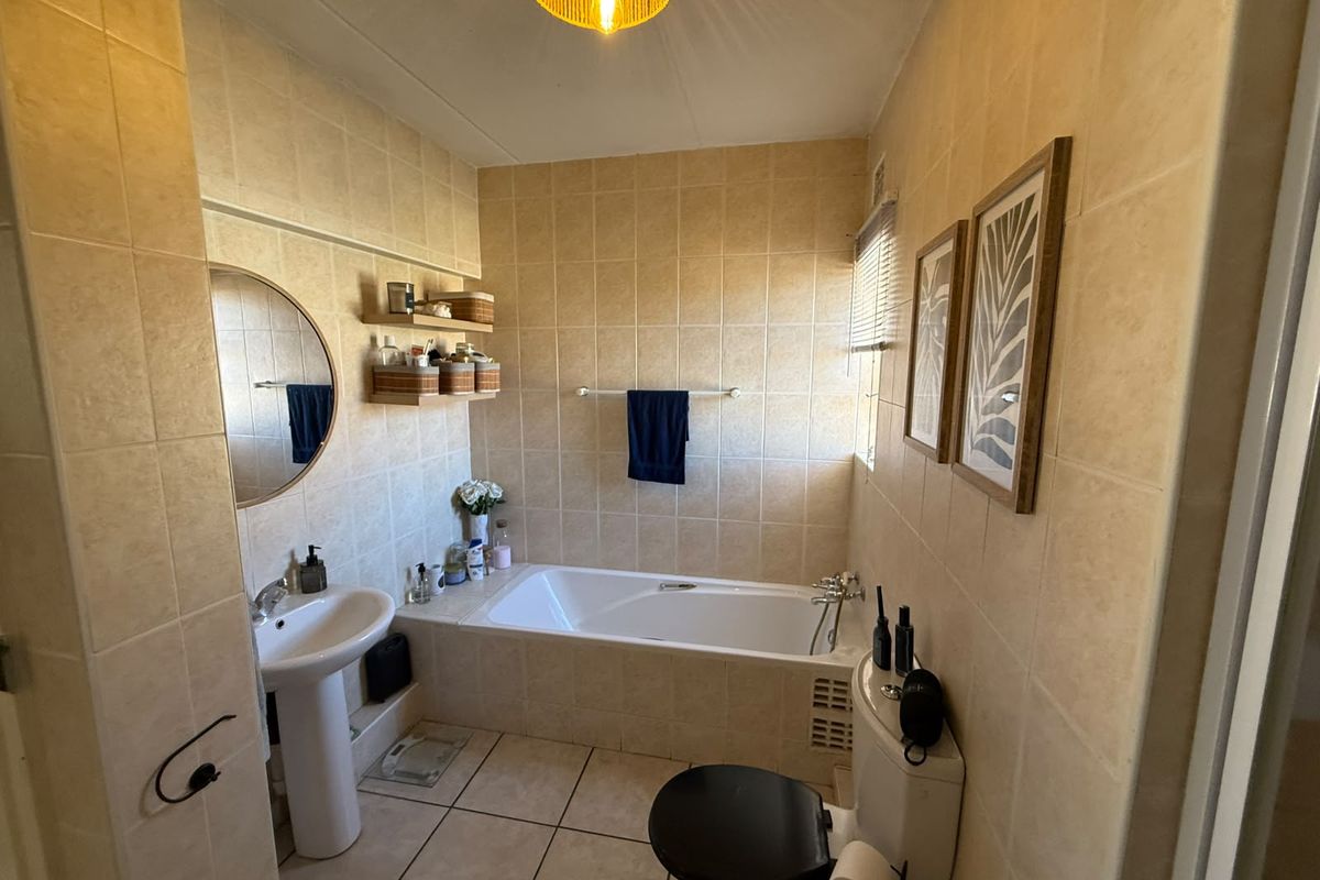 A functional bathroom featuring a pedestal basin, built-in bathtub, and toilet, finished with neutral ceramic wall and floor tiling.