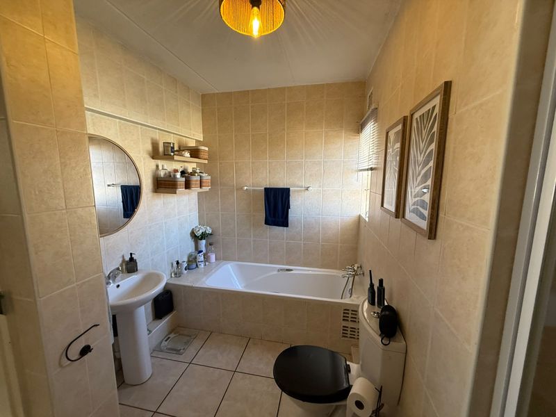 A functional bathroom featuring a pedestal basin, built-in bathtub, and toilet, finished with neutral ceramic wall and floor tiling.