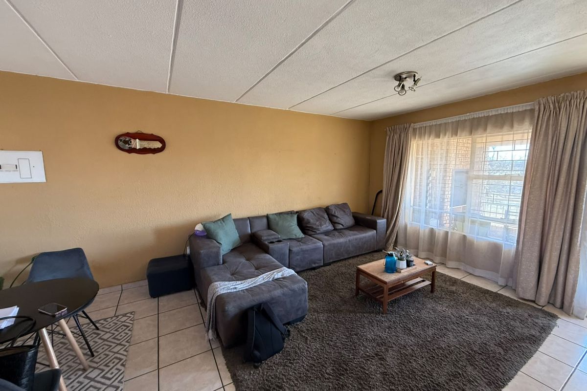 A living room featuring tiled flooring, a large window with curtains, and a neutral wall finish, offering a functional space for relaxation.