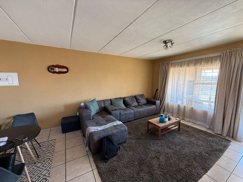 A living room featuring tiled flooring, a large window with curtains, and a neutral wall finish, offering a functional space for relaxation.