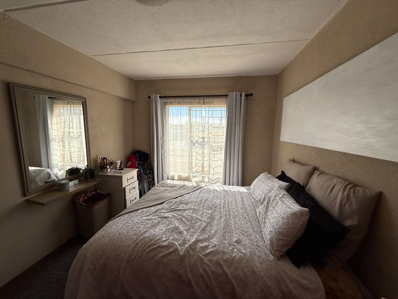 A bedroom featuring a sliding glass door with natural light, neutral wall finishes, and a wall-mounted shelf.
