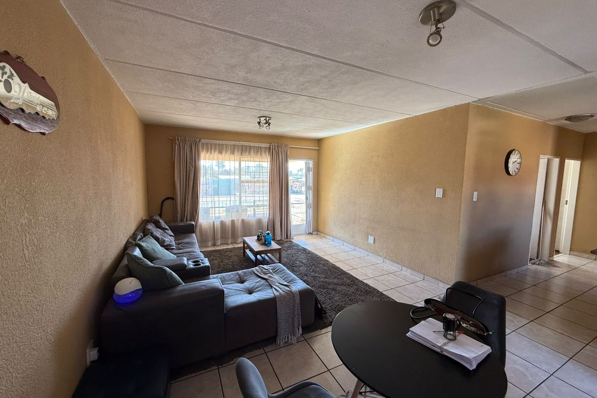 Open plan living and dining area featuring tiled flooring, textured walls, and direct access to an outdoor space through a security gate.