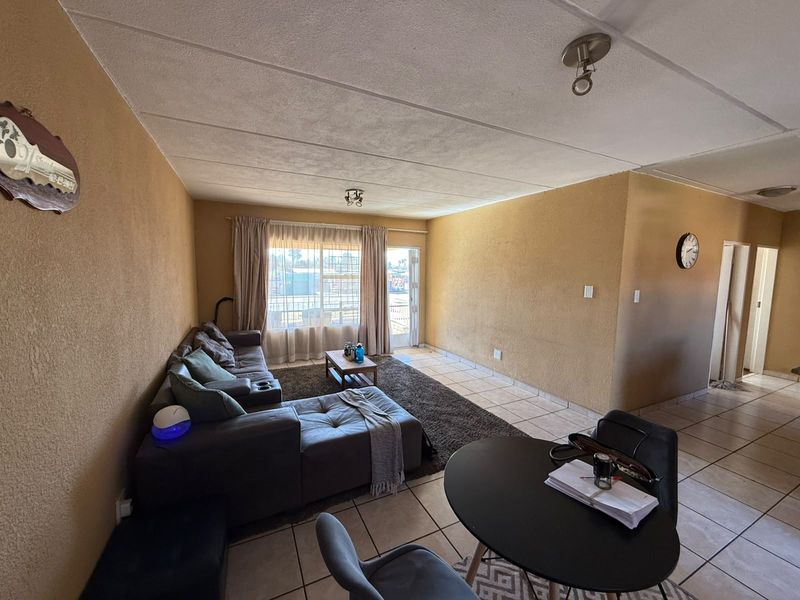 Open plan living and dining area featuring tiled flooring, textured walls, and direct access to an outdoor space through a security gate.