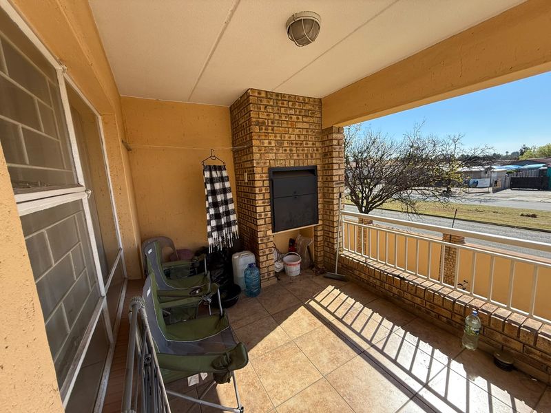 Covered balcony featuring a built-in brick braai, tiled flooring, and a metal balustrade, offering an outdoor entertainment space.