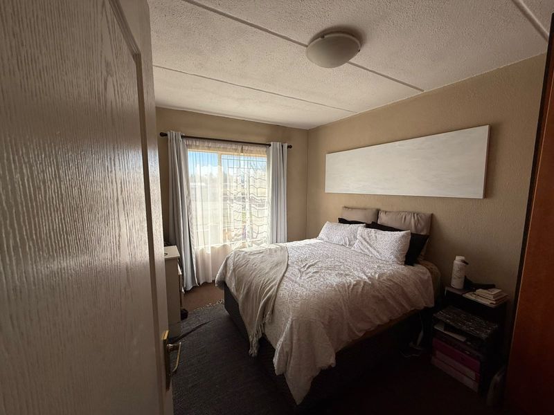 A standard bedroom featuring a built-in cupboard and neutral wall finishes, offering a functional space with natural light from the window.