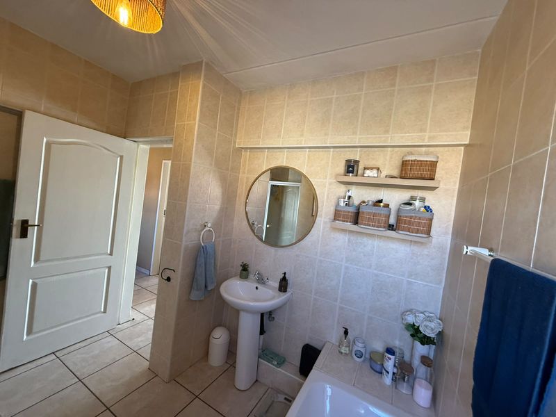A functional bathroom featuring tiled walls and flooring, a pedestal basin, and built-in wall shelving for storage.