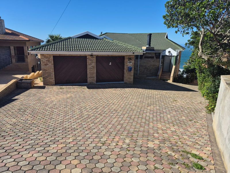Front exterior view of a brick house featuring a double garage, tiled roof, and a spacious paved driveway.