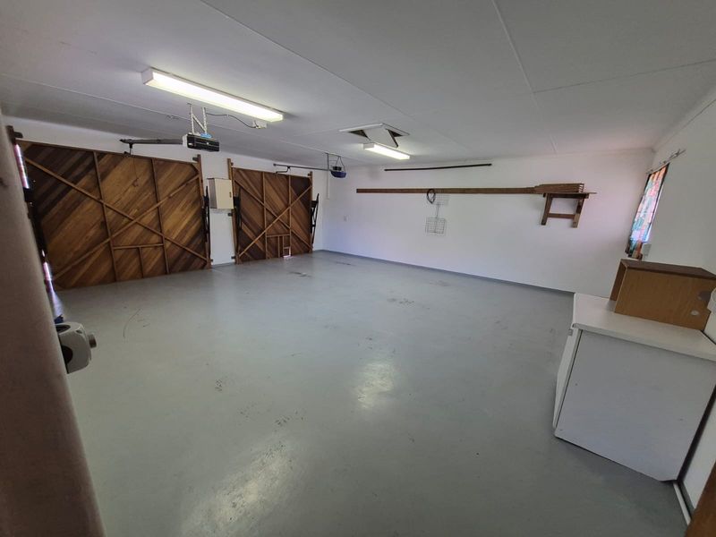 A spacious, empty double garage featuring painted concrete flooring, fluorescent lighting, and functional wall-mounted storage shelving.