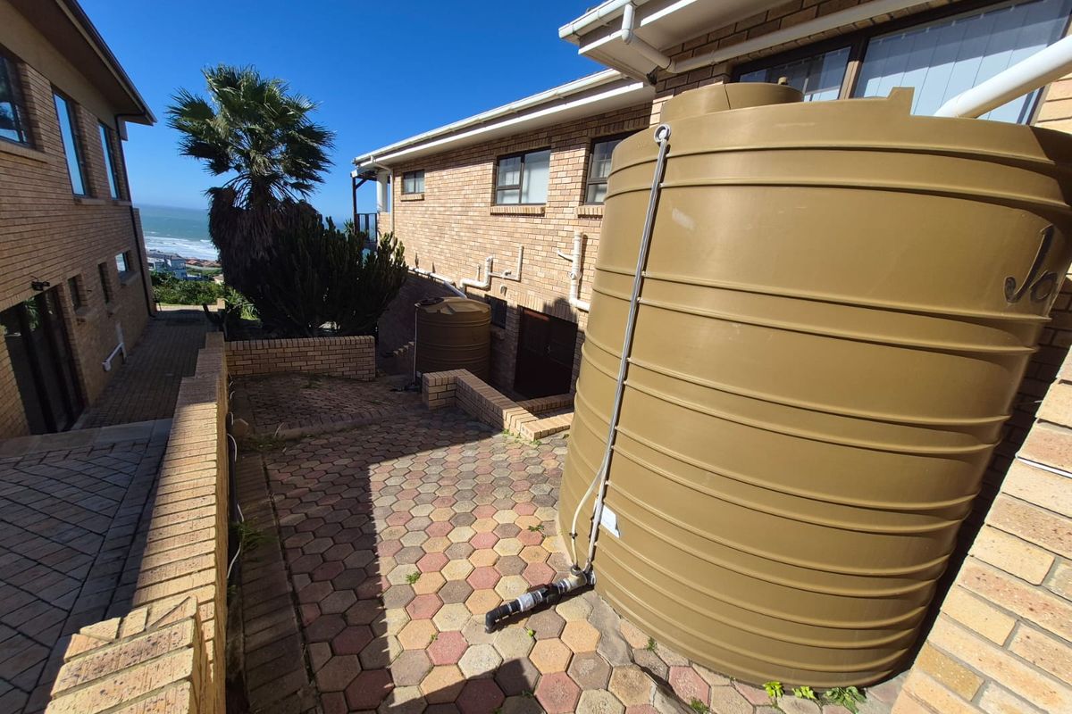 Rear exterior area featuring brick paving, retaining walls, and large water storage tanks connected to the building's guttering system.