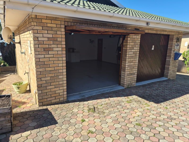 A double garage with brick exterior, tiled roof, and paved driveway, featuring one open bay and one closed wooden garage door.